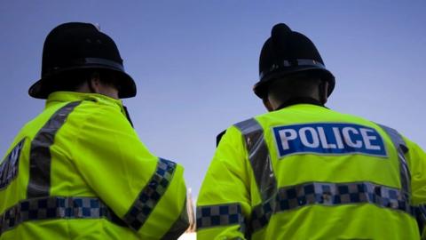 Two police officers stand next to each other wearing high-vis jackets and helmets