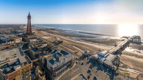 Aerial view of Blackpool's seafront showing North Pier, the beach and Promenade and Blackpool Tower on a sunny day.