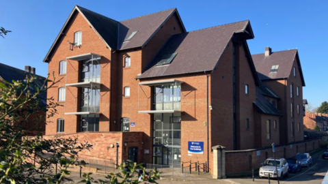 A large red brick building with a dark tiled roof and large glass windows