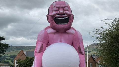 Giant inflatable man with hills and houses in background