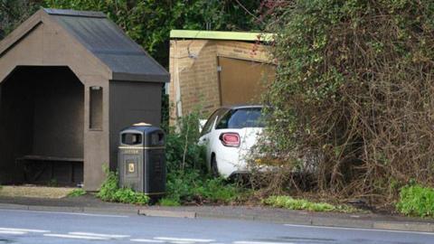 A car crashed into a gas substation in Pagham Road, near Nyetimber. The car is white and can be seen behind bushes and to the right of a bus stop.