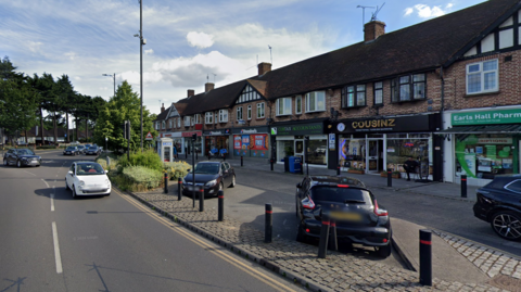 A general view of Earls Hall Parade, looking towards Victoria Avenue. A parade of shops are on the right, with the main road to the left.