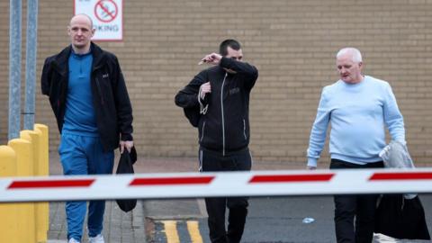 Three men leave the car park at HMP Barlinnie in casual clothing carrying black bags.