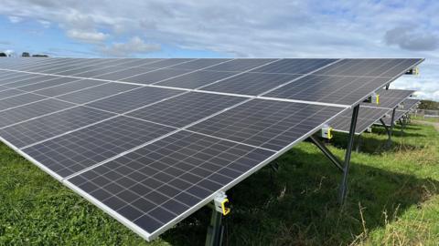 Solar panels in a field under a blue sky with white and grey clouds.