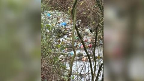 Rubbish including glass bottles and household waste is seen in the River Alt and on the banks of the river. 