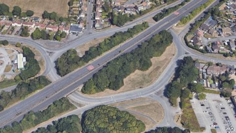 A dual carriageway with a large roundabout around it. It is a satellite aerial image.