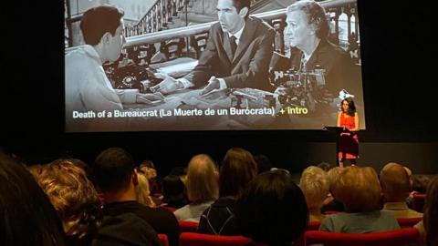 Founder Ketty Rodriguez introducing a screening of Cuban film, Death of a Bureaucrat in a cinema