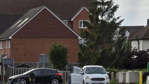 Two cars involved in a crash at a new junction on Meath Green Lane, Horley, Surrey. There is a white car facing forward and a black car which can be seen from the side.