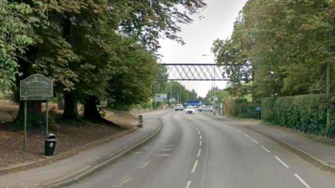 A street view of Melton Road in Thurmaston, showing a sign for Thurmaston Village on the left of the image. 