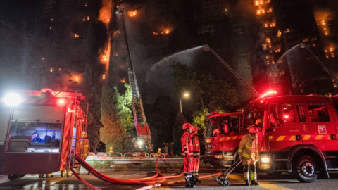 Firefighters stand next to a fire engine while tackling a blaze in Hong Kong