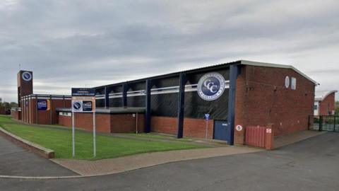 Churchill Community College. The school is made of red brick with blue supports.