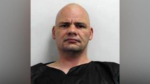 Police mug shot of Wayne Phillipson - a bald headed man wearing a black top