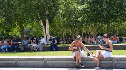 People sitting on concrete benches in the warm weather in Potters Fields Park, London.