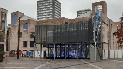 Culture House, photographed from Keel Square. It is a multi-storey brick building with a lot of windows. There is a large screen in front of it.