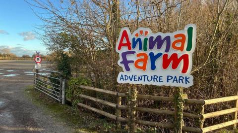 A brightly coloured sign outside of the farm which reads "Animal Farm Adventure Park."
