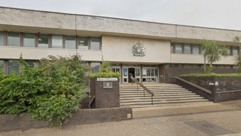 The outside of a crown court. There are shrubs and other greenery outside the building.