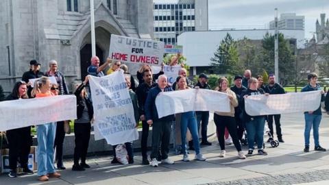 A group of about 20-30 people standing on a pavement, holding a protest in Aberdeen. One banner reads Justice for Homeowners