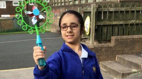 Shay Kang in a blue school uniform jacket holding up a bubble blower windmill toy