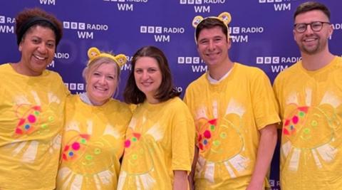 Presenters Trish Adudu, Kath Stanczyszyn, Sarah Julian and Dan Pallett and producer Matt Mitchell wear yellow t-shirts in front of a purple board with 91ȱ Radio WM branding. 