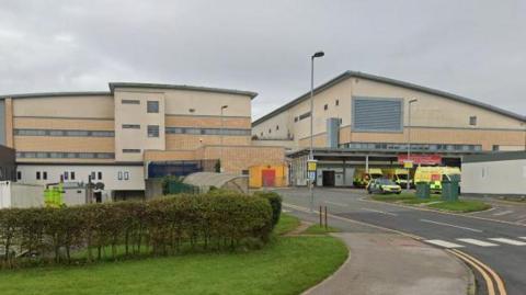 A street view of the exterior of the A&E department, where liveried ambulances are parked outside the entrance.