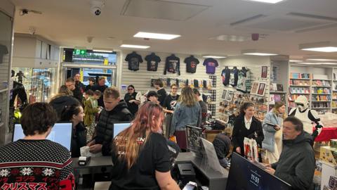 Customers busy shopping and looking around a science fiction shop with comics, figurines and merchandise on the wall.