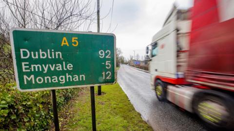 A road sign in Aughnacloy, Northern Ireland, for the A5, with a blurred moving lorry driving past