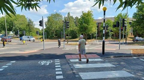 A man in shorts strutting across the road on the new zebra crossing