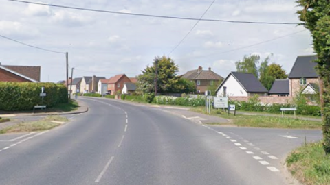 A road with a broken central white line curves off to the left. There is a junction to the right. Housing lines the right side of the road. 