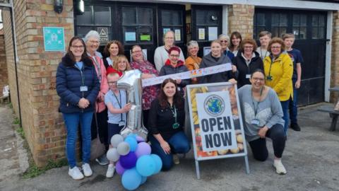 Group of people with a 1 balloon and a Open Now sign 