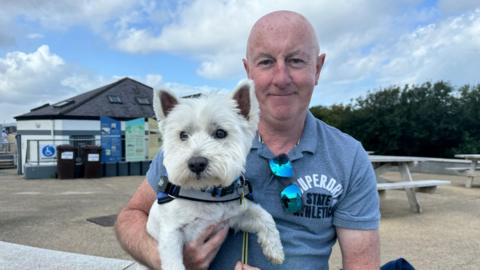 A man in a blue t shirt holding his small white dog