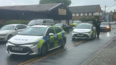 Two parked police cars and an officer by the pavement in a residential street.