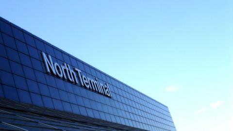 An image showing the top of the North Terminal building at Gatwick airport, it is dark blue glass and the sky behind is blue