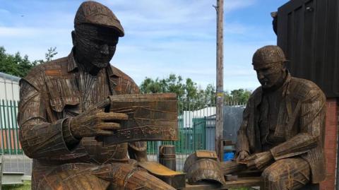 A sculpture of shipyard workers on their lunch break reading The Echo