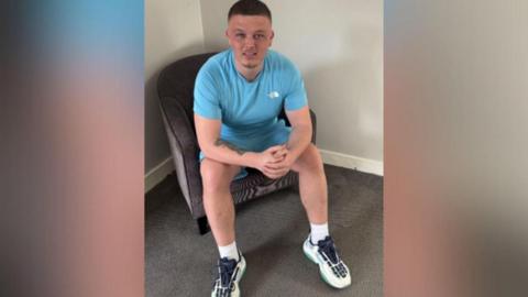 Image of Dale Martin. He is sat on a chair and is wearing a sky blue t-shirt and shorts.