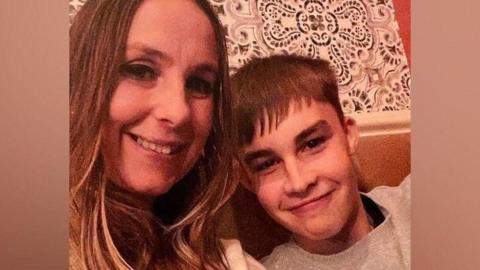 Max Dixon with his mum Leanne. They are sitting on a sofa and both are smiling directly at the camera.