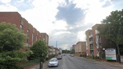 Blocks of housing either side of a road with cars parked on kerb