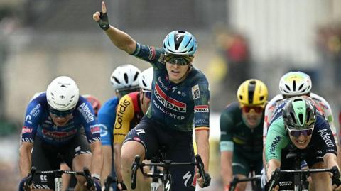 Tim Merlier celebrates winning stage 12 by raising a finger into the air