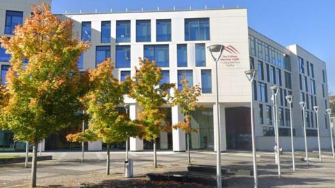 A four storey building has a sign saying 'The College Merthyr Tydfil' and 'Y Coleg Merthyr Tudful'.