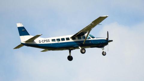 A blue and white Cessna plane with the serial number G-CPSS on the site. Its wheels are down and there is a propeller at the front.