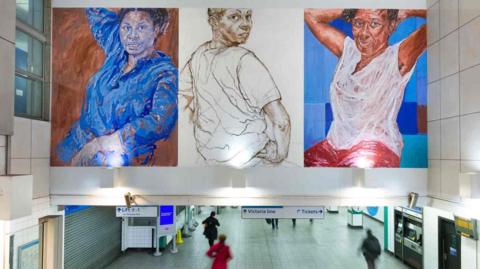 Three large artworks installed above the concourse at Brixton tube station. They depict three women in various poses, looking at the viewer. 