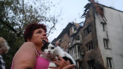 A woman holds a cat in front of a building in Kyiv hit by a Russian shell on 10 July