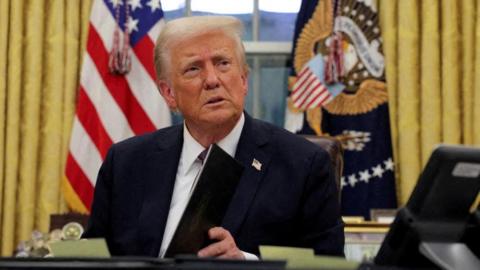 Donald Trump signs documents in the Oval Office