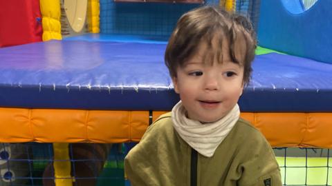 Artemis Sanson is seen a soft play area wearing a green zip up jumper with a striped neckerchief 