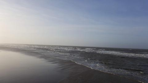 Blackpool beach - the tide is going out as the sand is wet, it appears to be dusk as the sky is a blue with the light of a sunset creeping in.