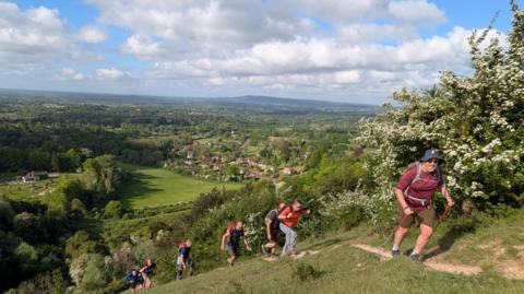 A group of men climb up a very steep hill that overlooks a small village. 