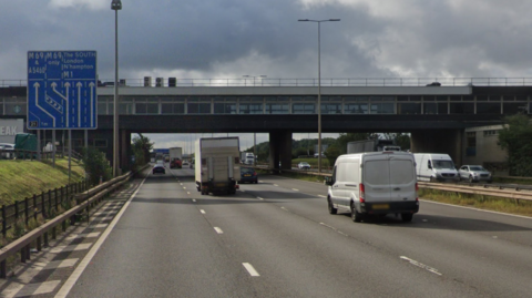 Google Streetview image of the M1 southbound carriageway near junction 21 with cars, vans and lorries passing underneath a bridge