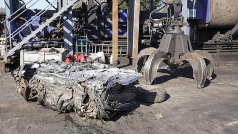 the remains of a silver car that was crushed in a scrap yard