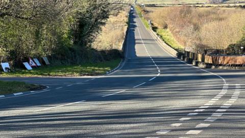 Hillberry Corner, a well-maintained road which has a sharp corner, the road is surrounded by fields.