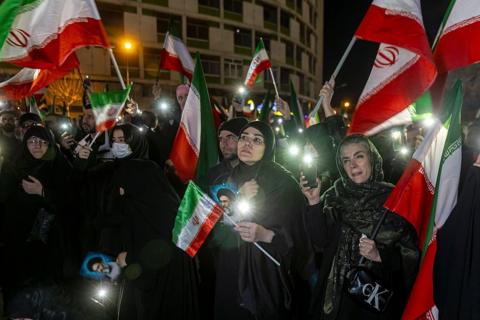 People in a crowd, some holding Iranian flags and images of the country's leader Ayatollah Ali Khamenei.