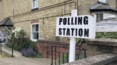 A black writing and white background sign says "polling station" in capital letters, it has been put up outside a church building.